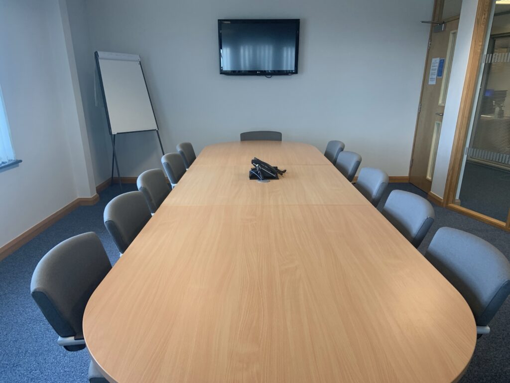 Long Boardroom style table with a large TV on the wall.