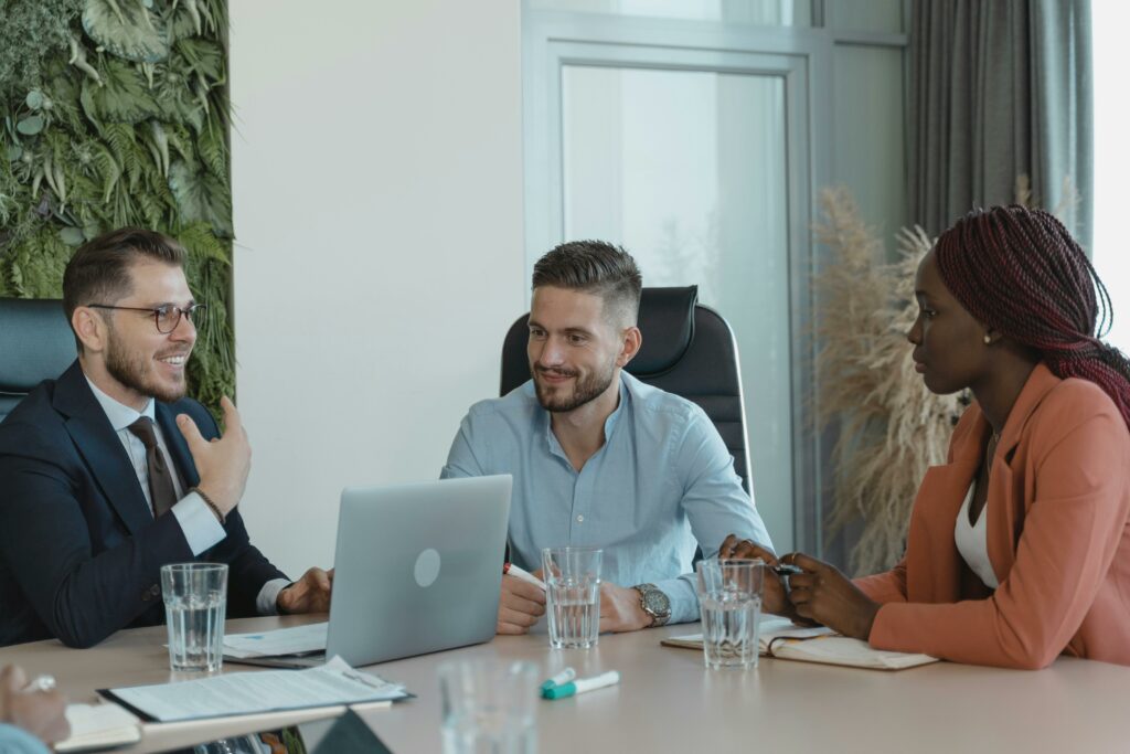 3 people around a table having a meeting on a laptop.